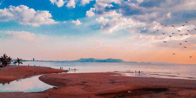 Pastel-toned travel scene at golden hour with warm sand, calm water, and soft pink sky