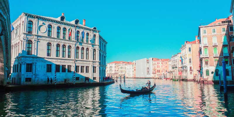 Canal scene with a gondola on blue-green water beside historic multi-story buildings under a clear blue sky